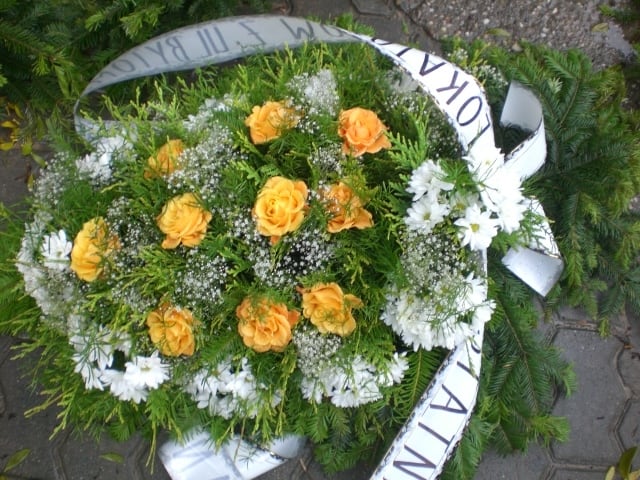 wiązanka pogrzebowa ze świeżych białych i pomarańczowych kwiatów z napisem na szarfie