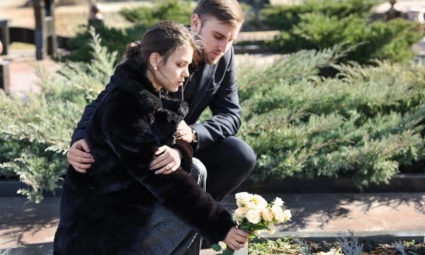 Dwoje młodych ludzi na cmentarzu podczas składania kwiatów na grób bliskiej osoby