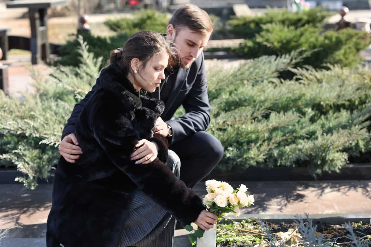 Dwoje młodych ludzi na cmentarzu podczas składania kwiatów na grób bliskiej osoby