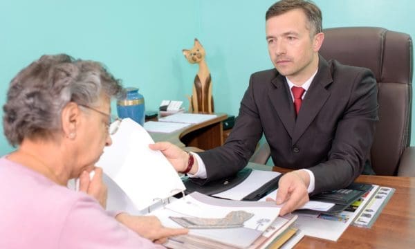 pracownik zakładu pogrzebowego pomaga wybrać starszej kobiecie nagrobek z firmowego katalogu